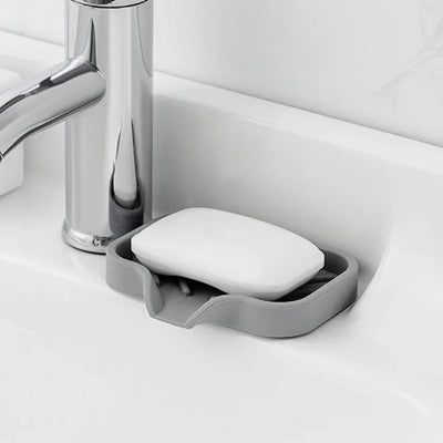 Silicone Sink Tray – Soap & Sponge Holder with Drain next to a faucet holding a bar of soap.