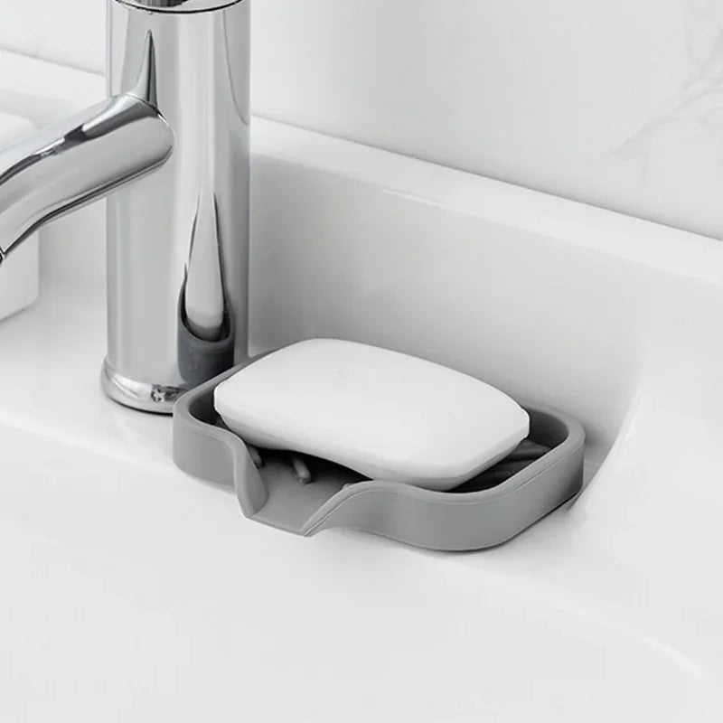 Silicone Sink Tray – Soap & Sponge Holder with Drain next to a faucet holding a bar of soap.